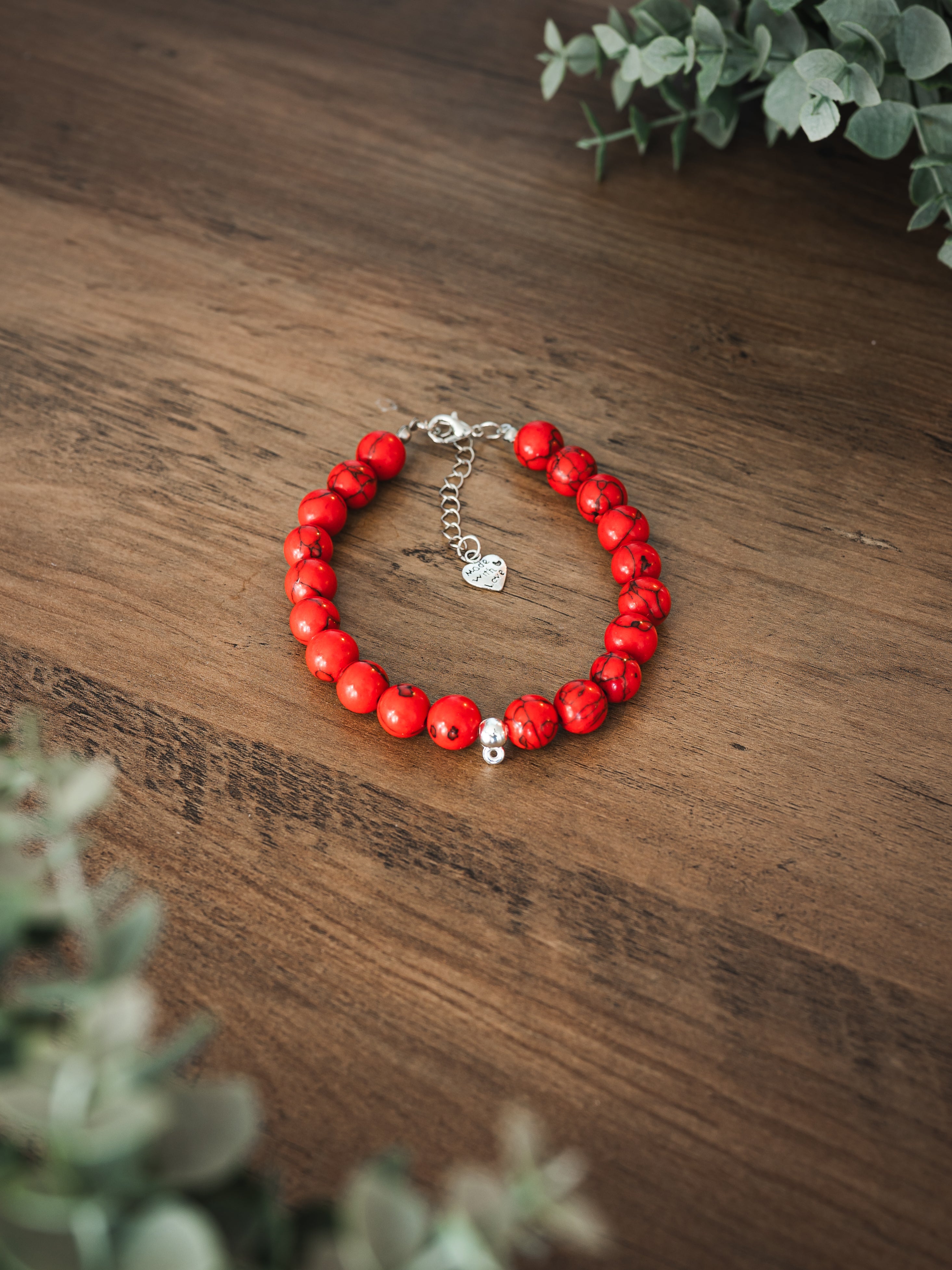 Red howlite stone pet necklace with natural black veining and heart Made with Love charm on a wooden surface