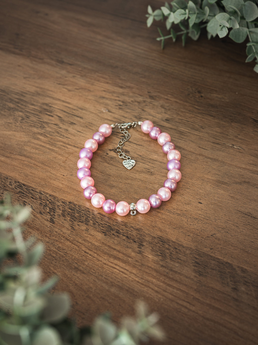 Pink and purple faux pearl pet necklace with heart Made with Love charm on a wooden surface