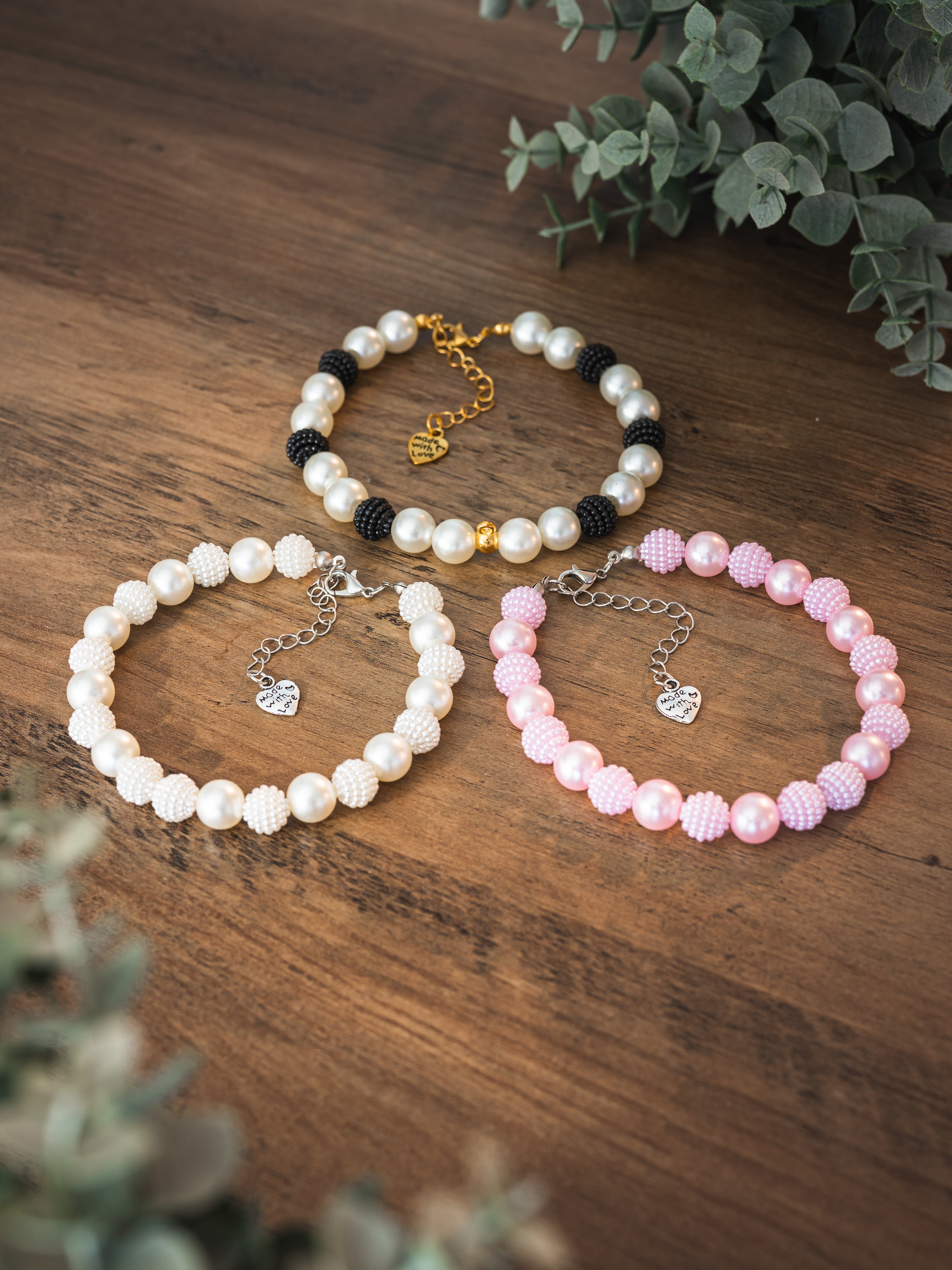 Mixed pearl and textured faux pearl pet necklaces in white, pink and black with heart Made with Love charm on a wooden surface