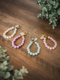 Faux pearl keychains in white, pink, and blue with crystal charm and gold or silver clasp on a wooden surface