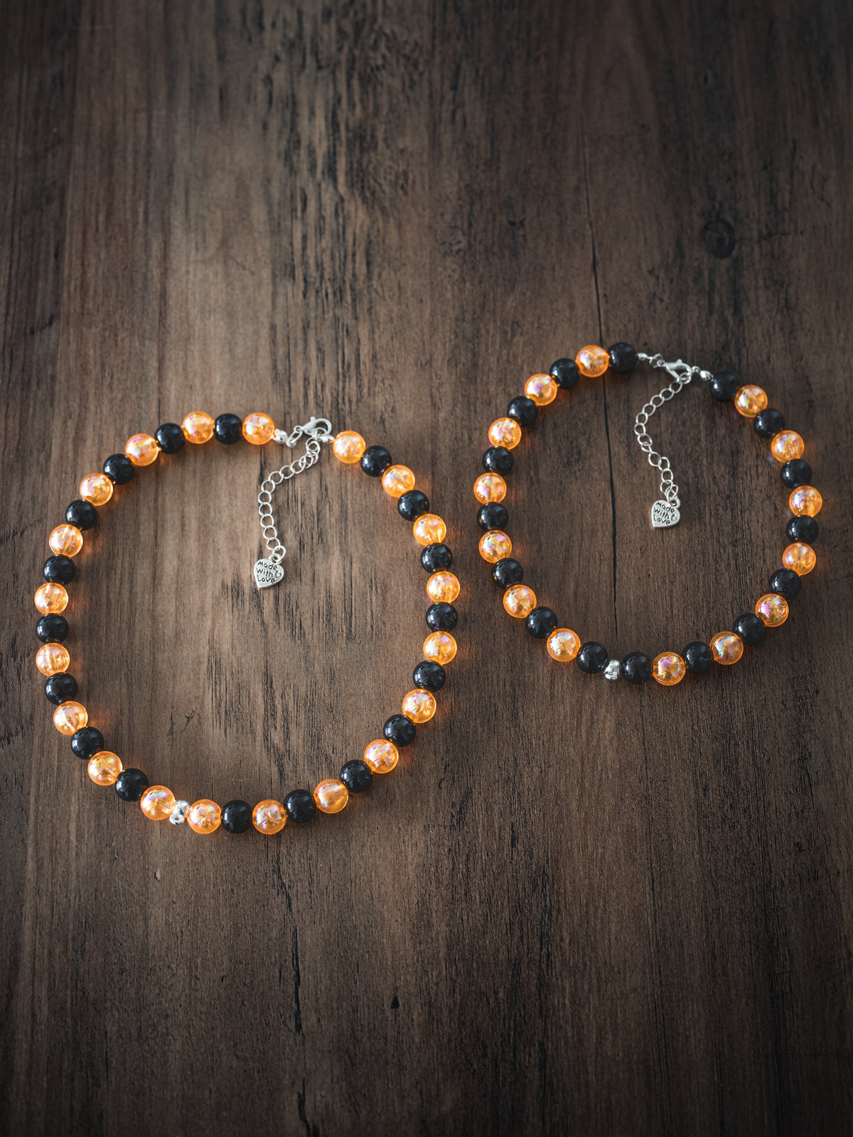 Two Halloween pet necklaces with alternating black and orange beads on a wooden surface