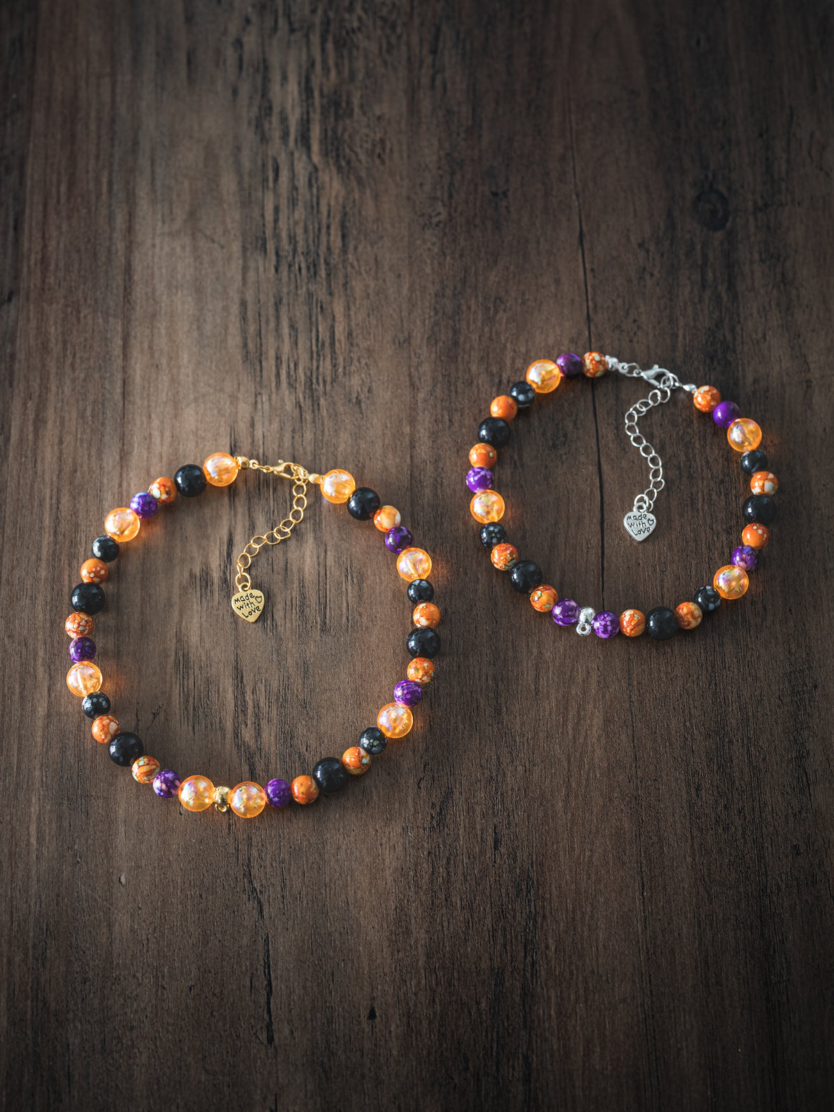 Two Halloween pet necklaces with mixed purple, orange and black beads in varying sizes on a wooden surface, one with gold chain and one with silver chain