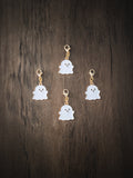 Four white enamel ghost charms with gold lobster clasps arranged on a dark wooden surface